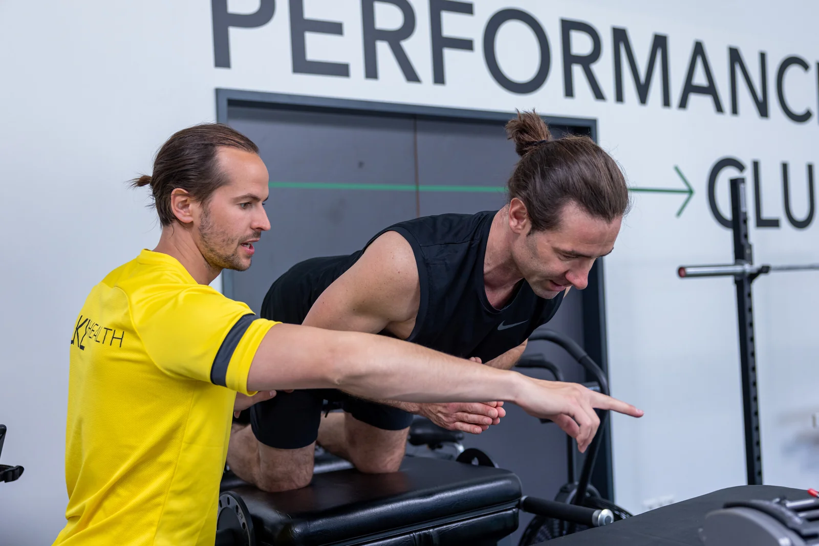 Coach erklärt einem Kunden eine Übung vor der Performance-Club-Wand