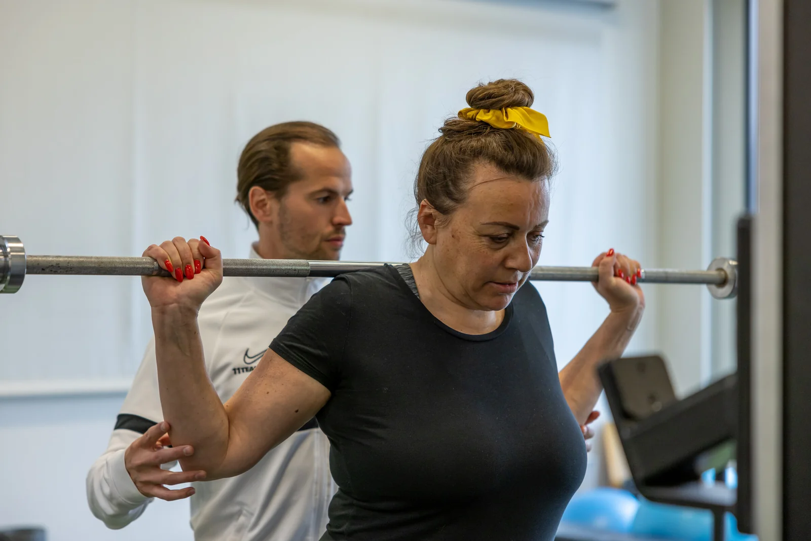 Coach sichert eine Klientin bei einer Übung mit der Langhantel